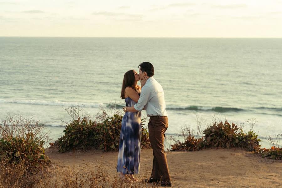 Dylan and Jessica kissing on the bluff with the ocean behind them