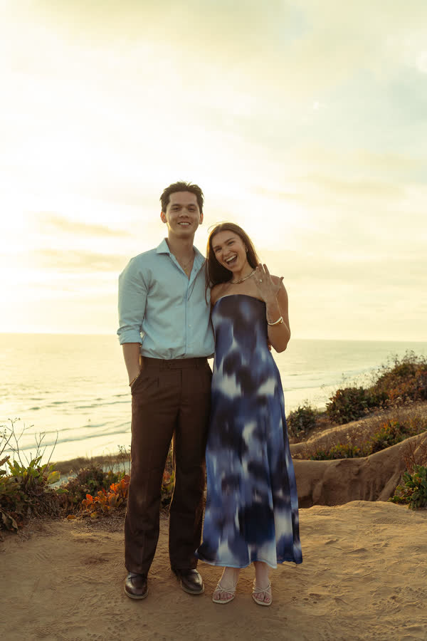 Dylan and Jessica smiling at the camera as Jessica shows her ring at sunset