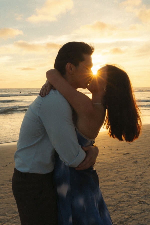 Dylan and Jessica kissing on the beach with the sun bursting between them