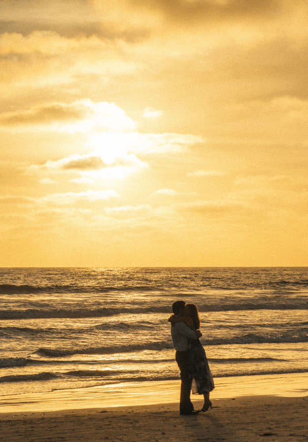 Dylan and Jessica silhouetted in an embrace at the water's edge under a golden sky